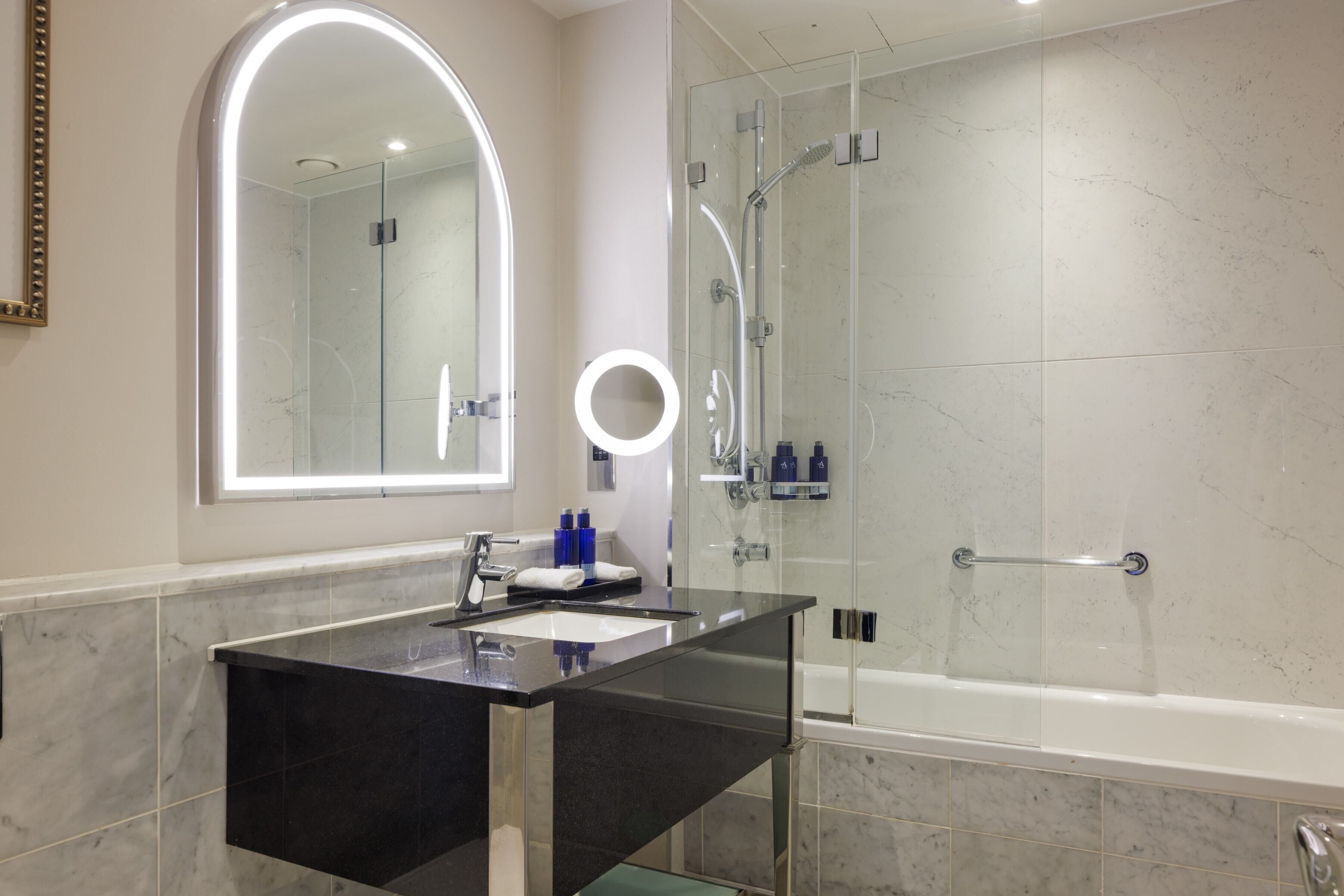 A modern bathroom with a glass-enclosed shower, a black vanity with a large mirror, and a round light fixture above the mirror.