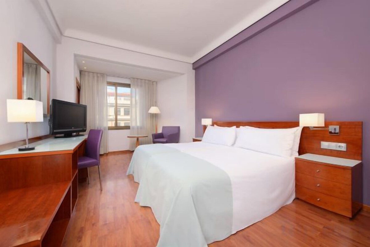 Een hotelkamer met een bed, nachtkastjes, een bureau met een televisie en een stoel.