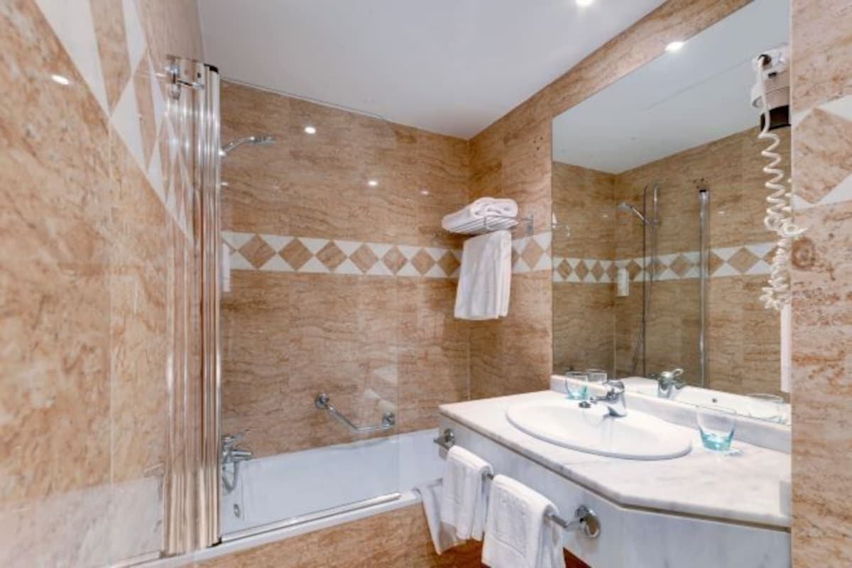 A bathroom with a glass shower enclosure, a bathtub, a sink with two mirrors, and a towel rack.