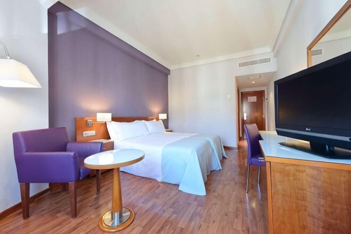 Een hotelkamer met een bed, een televisie, een klein tafeltje en een paarse stoel.