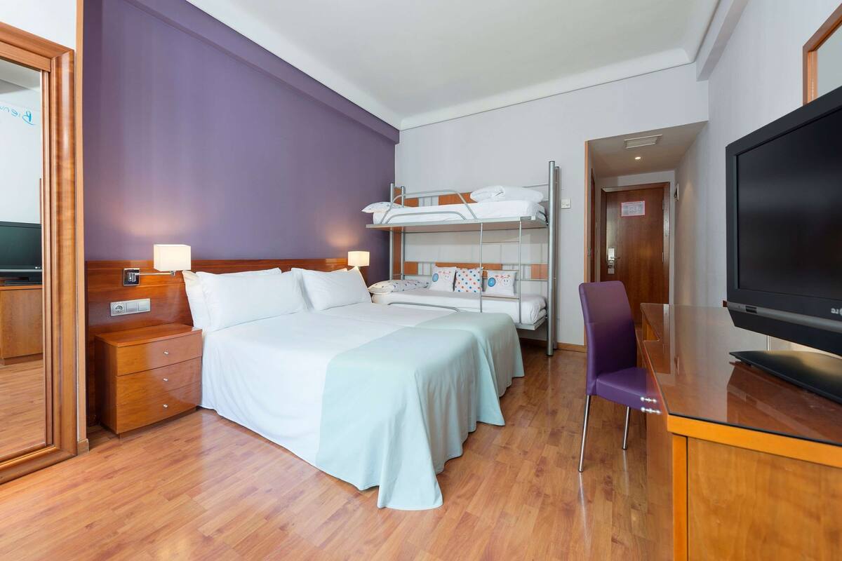 Ein Hotelzimmer mit einem Bett, einem Schreibtisch, einem Fernseher und einem Etagenbett.