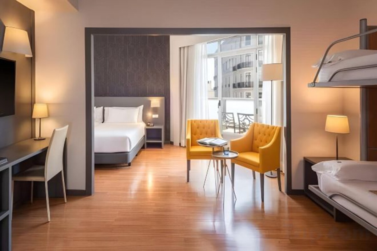 Ett hotellrum med en säng, ett skrivbord, en stol, ett litet bord och en våningssäng.