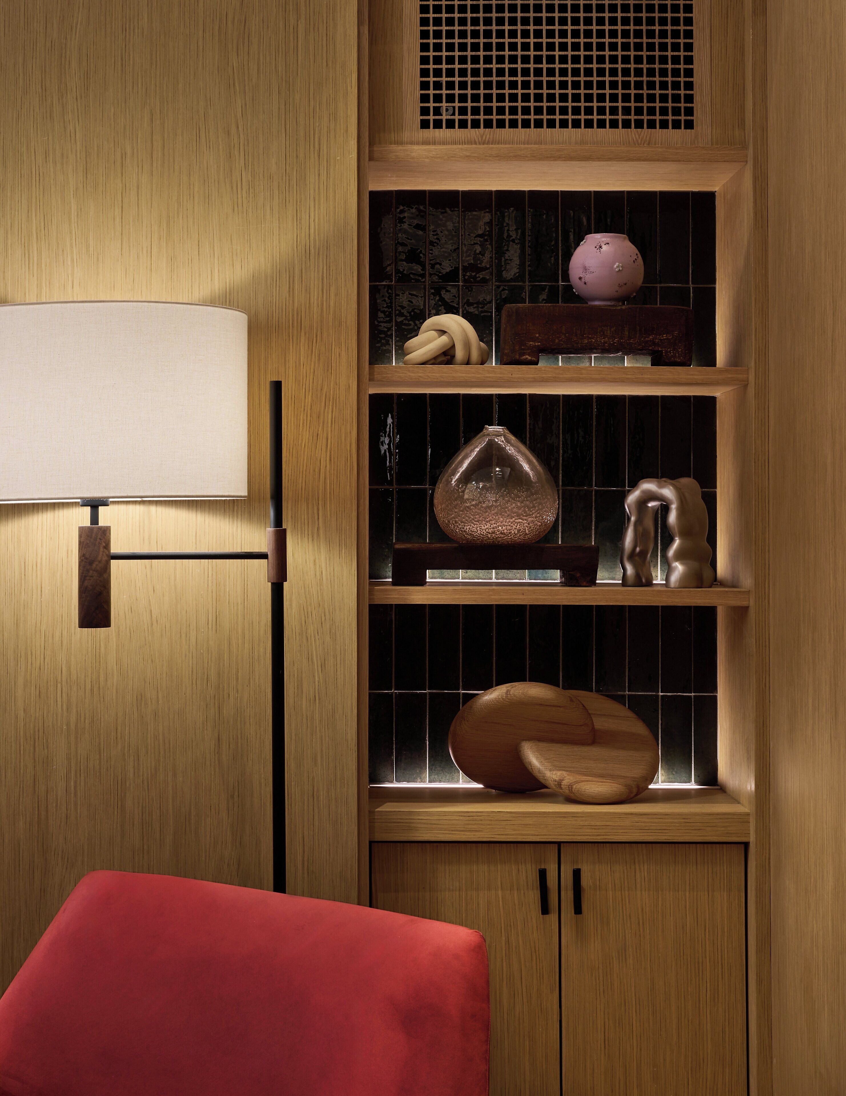 A wooden cabinet with shelves containing various decorative items, a red chair, and a wall-mounted lamp.
