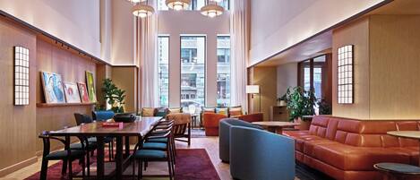 A spacious lobby with a wooden floor, a central dining table with chairs, a blue sofa, and a leather couch.
