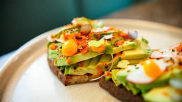 Een plak toast met avocado, ei en groenten op een bord.