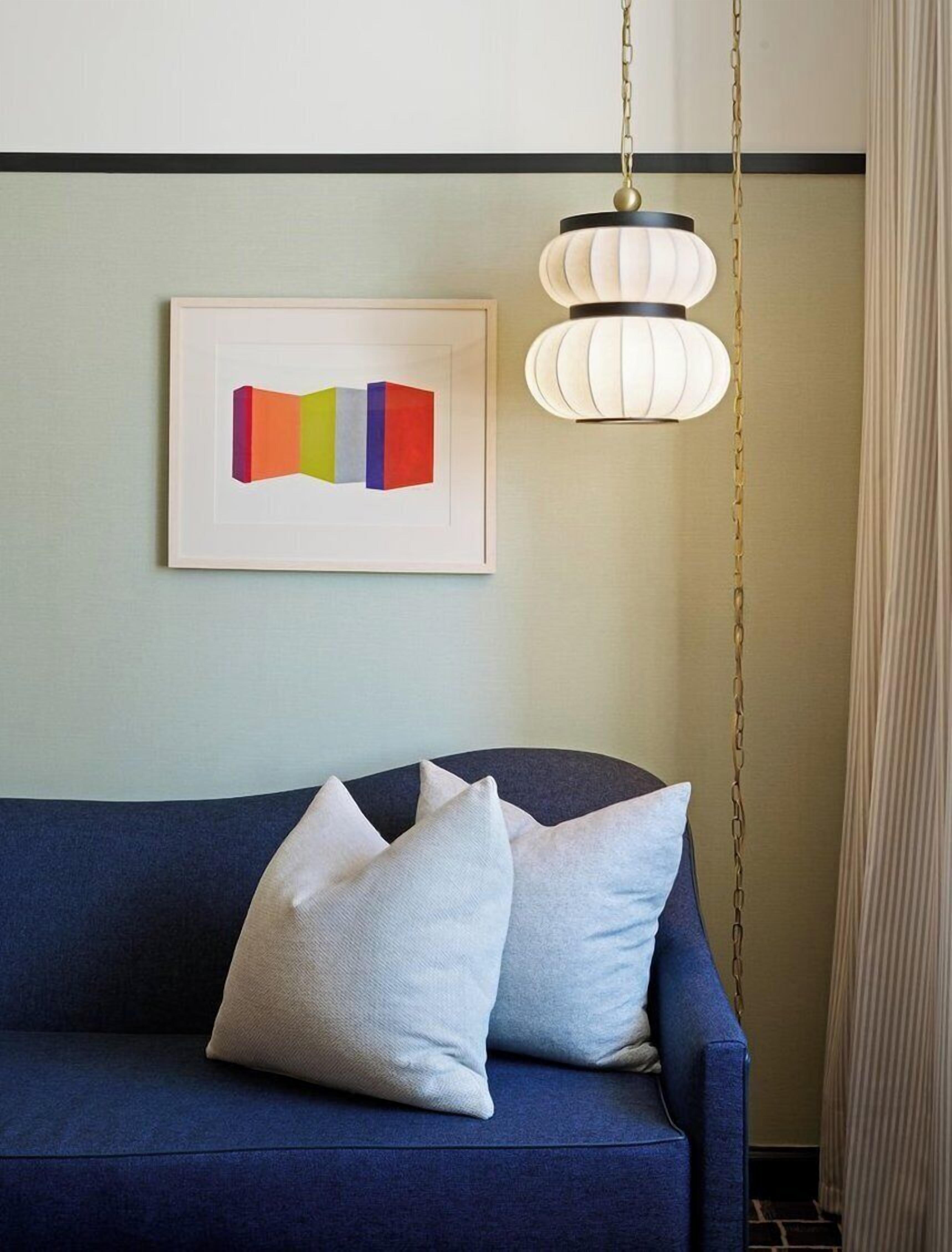 Un canapé bleu avec des coussins blancs, une œuvre d’art abstraite encadrée et une suspension lumineuse.
