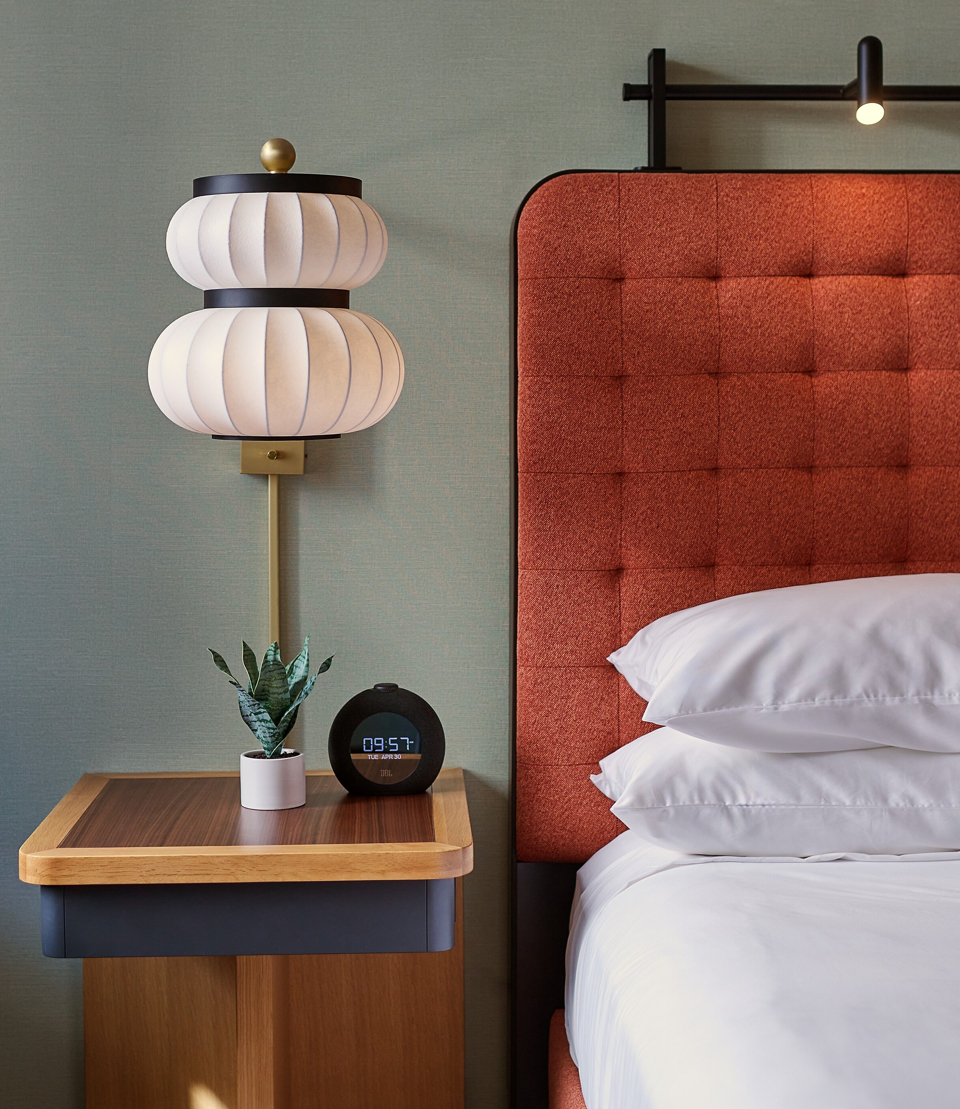 A neatly made bed with white linens, a bedside table with a lamp, and a digital clock displaying the time.