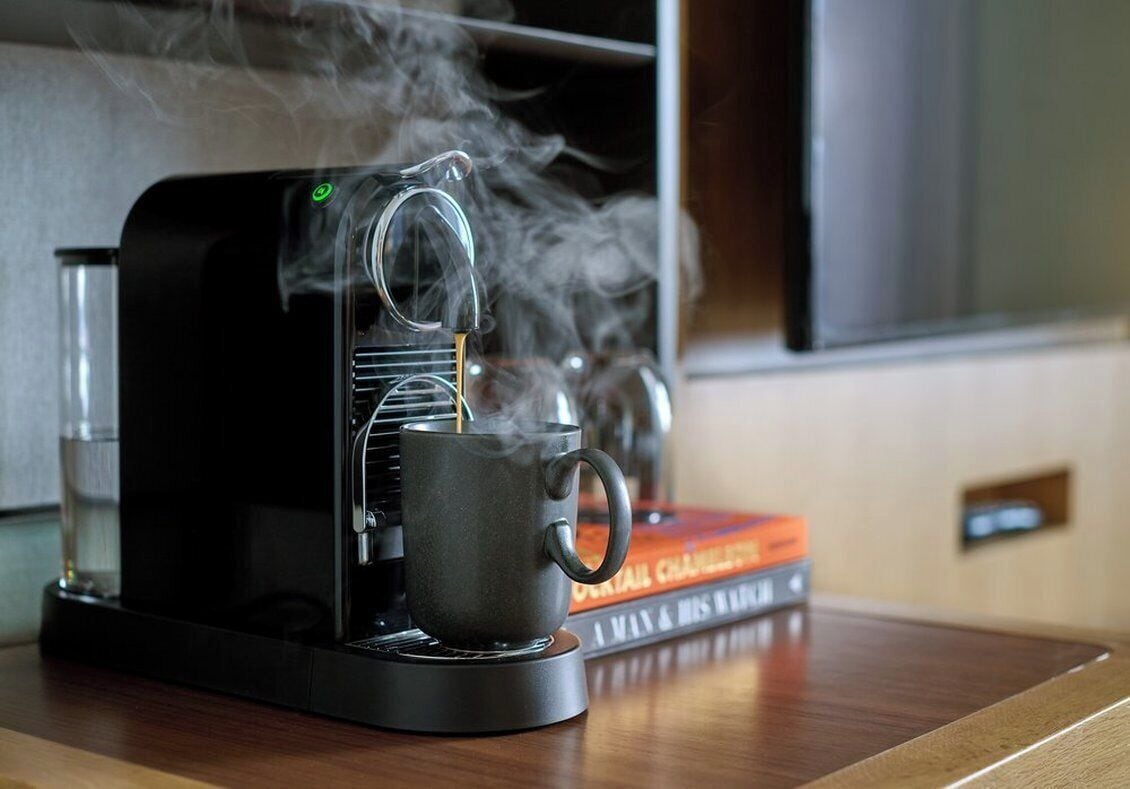 Una cafetera emitiendo vapor, una taza negra y un libro titulado 