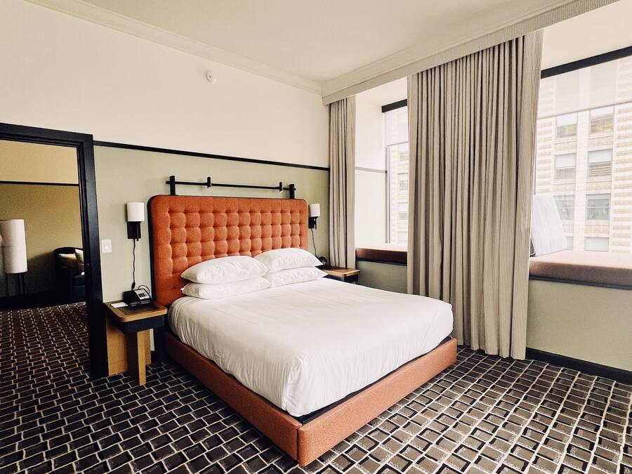 A hotel room with a large bed, a nightstand, a mirror, and a window with curtains.