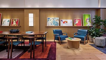 Un área de descanso moderna con una mesa de madera, sillas azules, una mesa redonda de centro y obras de arte en las paredes.