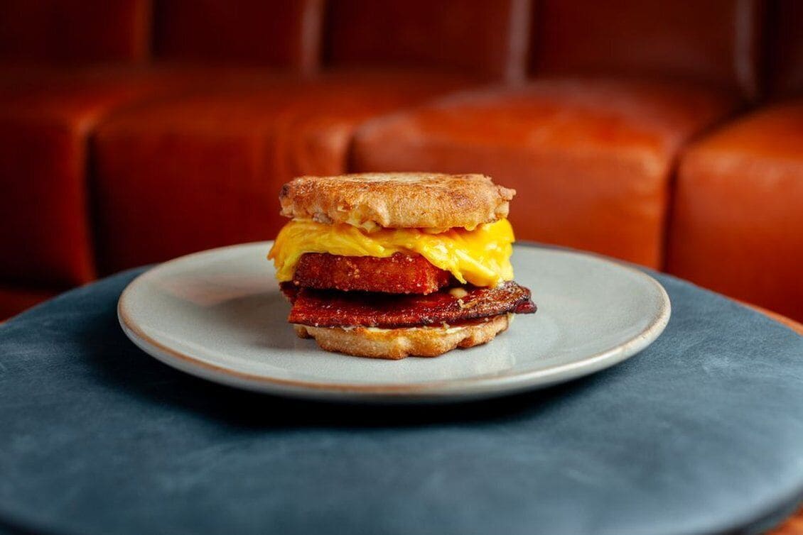 A breakfast sandwich on a plate with a dark table and a red leather couch in the background.