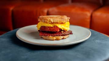 A breakfast sandwich on a plate with a dark table and a red leather couch in the background.