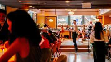 A restaurant interior with tables and chairs, a bar area, and a counter where waitstaff are serving.