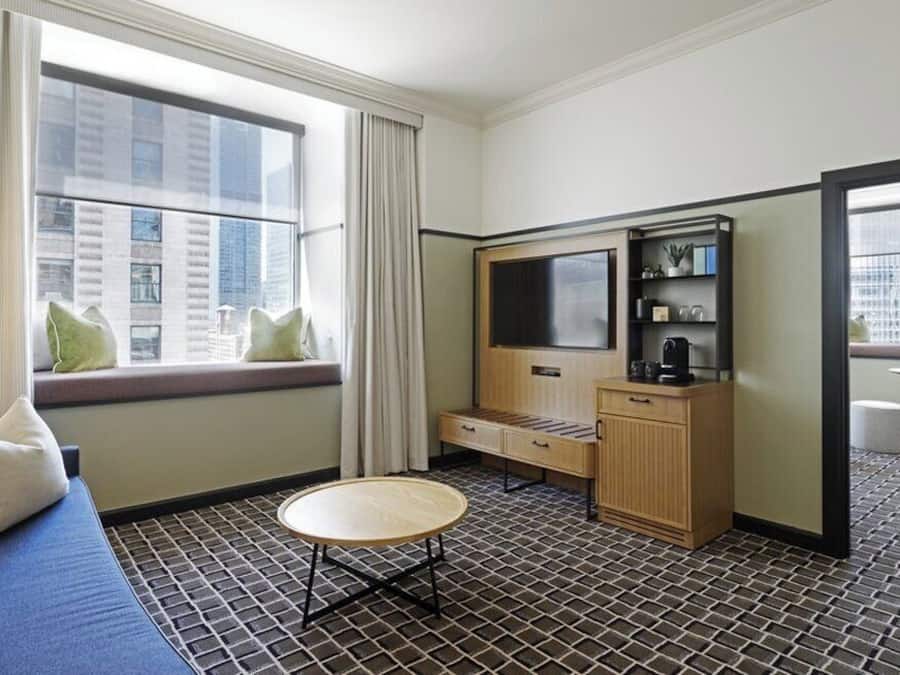 Hotelkamer met een bank, een klein rond tafeltje, een televisie, een kast en een raam met uitzicht over de stad.