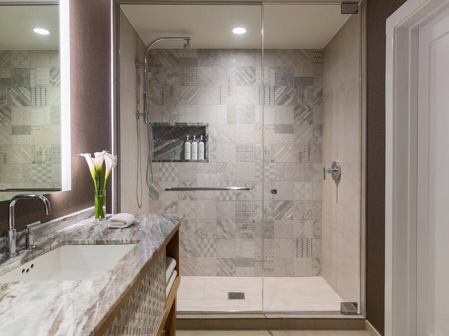Uma casa de banho moderna com chuveiro envolto em vidro, lavatório de mármore e um nicho embutido com artigos de higiene pessoal.