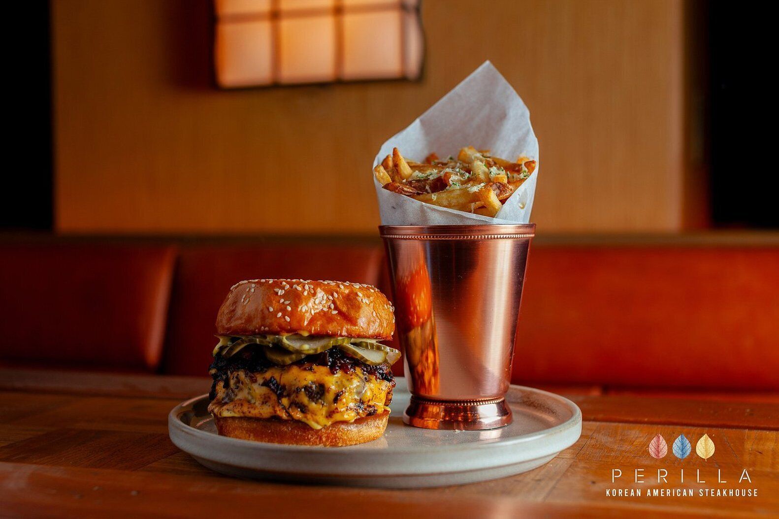 A burger and fries on a plate with a copper cup, in a restaurant setting.