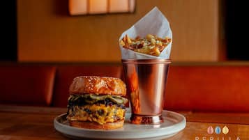 A burger and fries on a plate with a copper cup, in a restaurant setting.