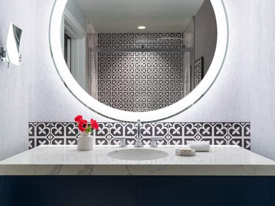 Un baño con un espejo redondo, un lavabo y un salpicadero decorado.