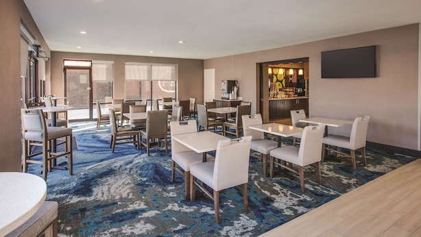 A hotel dining area with multiple tables and chairs, a bar area, and a large window providing a view of the outside. - La Quinta Inn & Suites by Wyndham Philadelphia Airport (Essington)