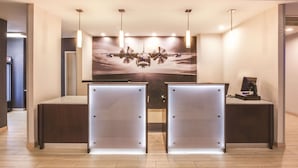 A reception area with a large poster of a helicopter, two reception desks, and pendant lighting. - La Quinta Inn & Suites by Wyndham Philadelphia Airport (Essington)