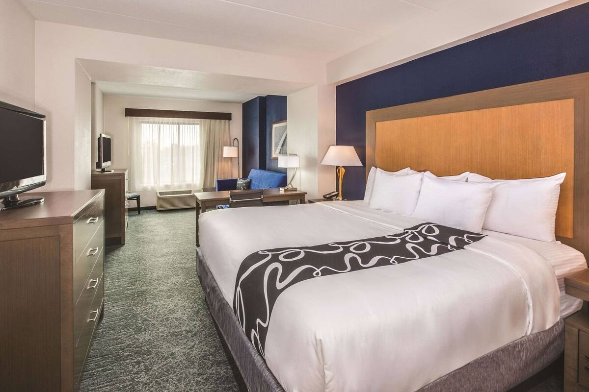 A hotel room with a large bed, a desk, a television, and a chair.