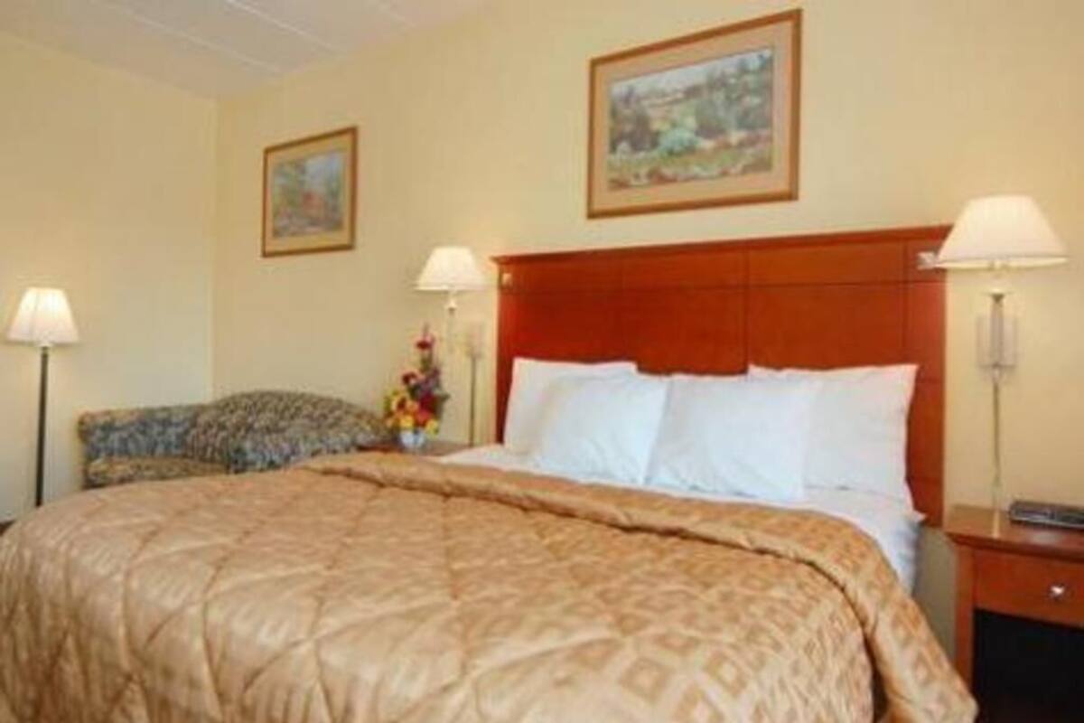 Une chambre d’hôtel avec un grand lit, deux tables de chevet, une tête de lit et deux lampes fixées au mur.