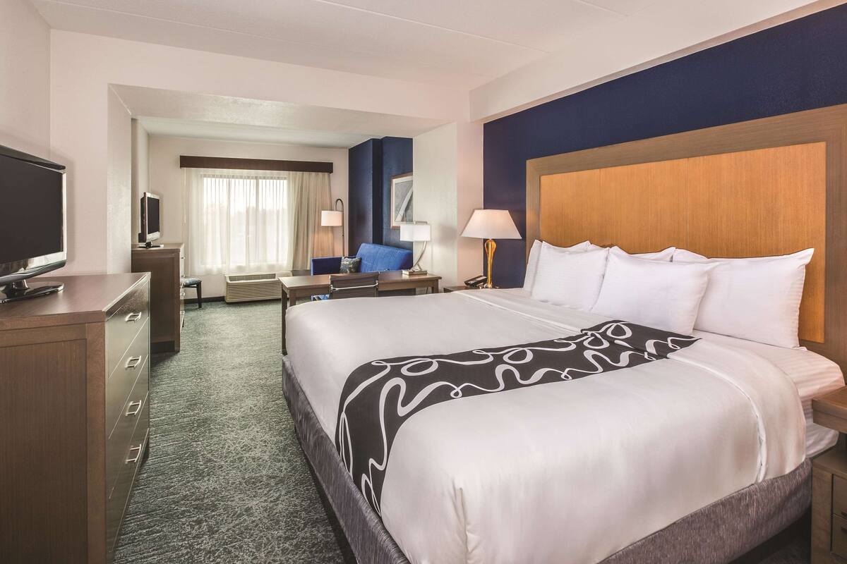 Une chambre d’hôtel avec un grand lit, un bureau avec un ordinateur, une télévision et une fenêtre avec des rideaux.