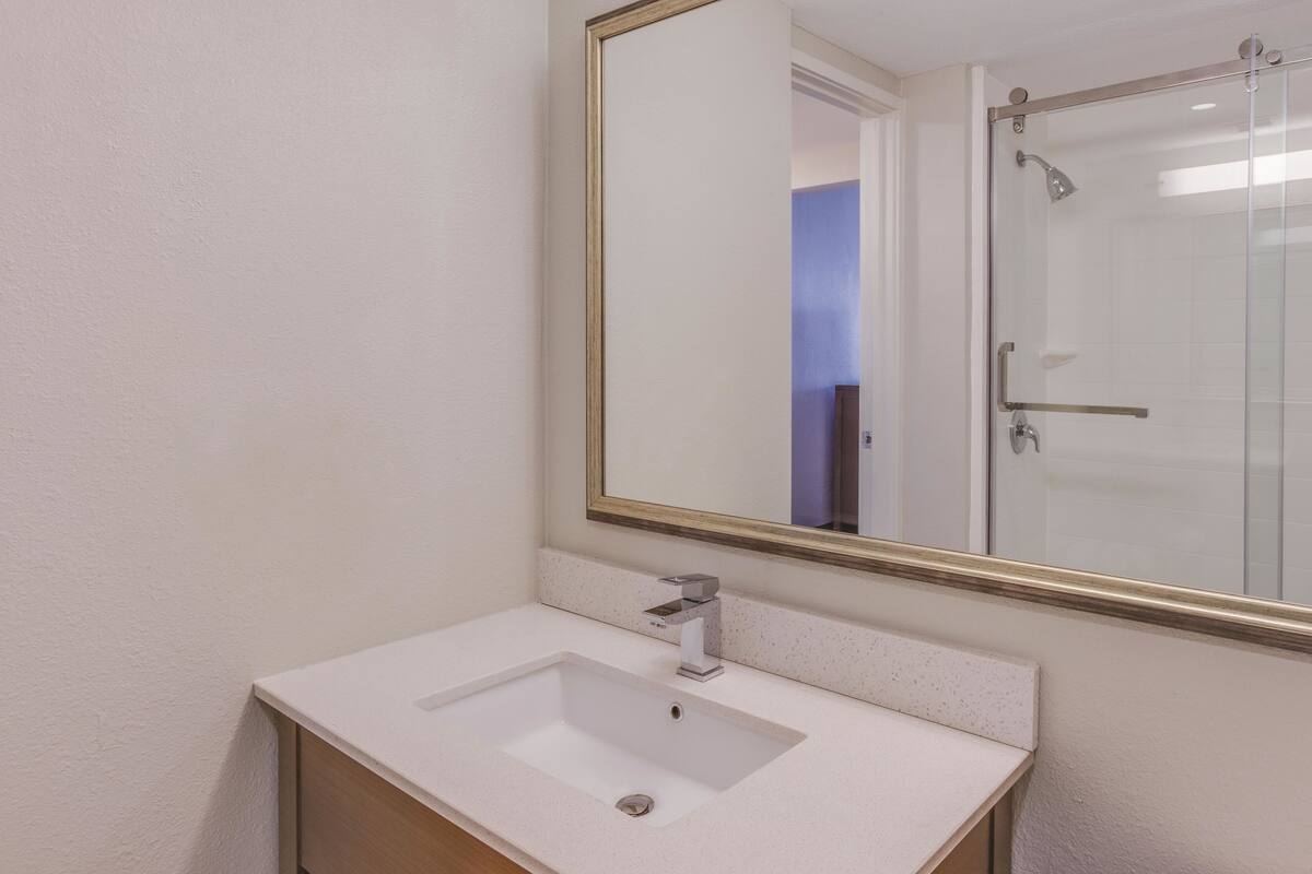 Une salle de bain avec un lavabo blanc, un grand miroir et une cabine de douche en verre.