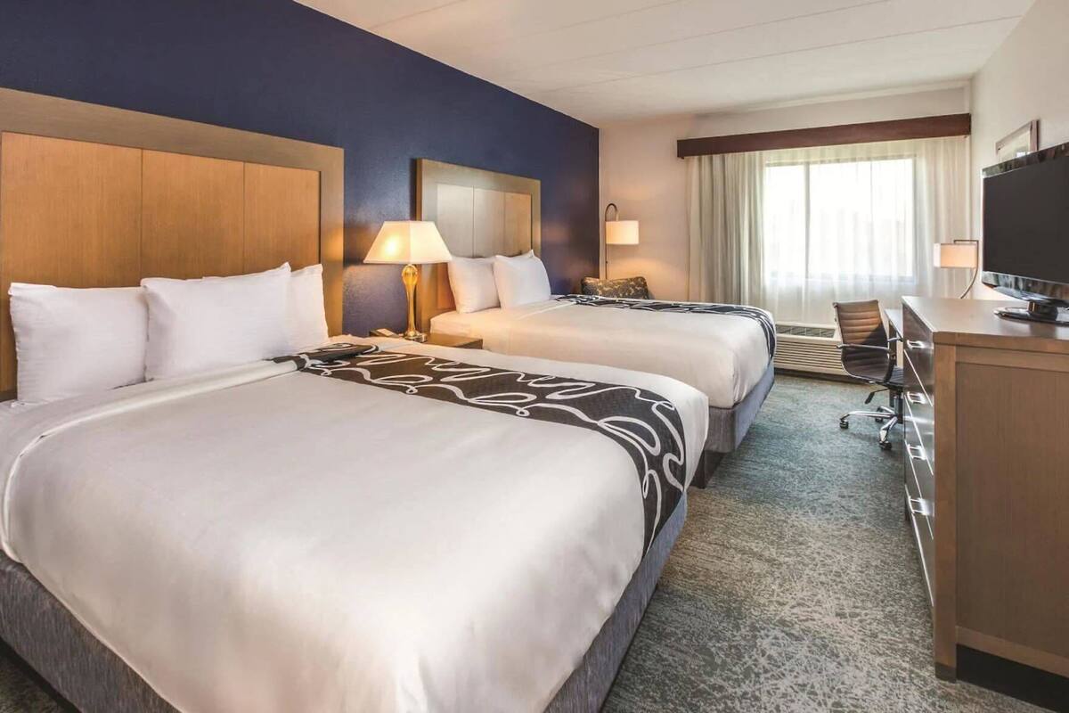 Une chambre d’hôtel avec deux lits, un bureau avec une télévision et une fenêtre avec des rideaux.