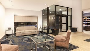 A modern living room with a sofa, armchairs, a glass coffee table, and a large glass door leading to a kitchen. - La Quinta Inn & Suites by Wyndham Philadelphia Airport (Essington)