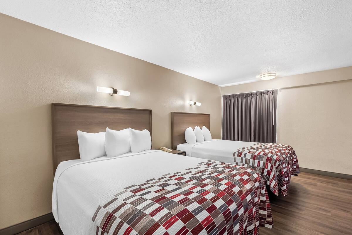A hotel room with two beds, each with a different style of bedding, and a large window with curtains.