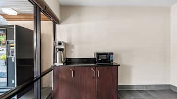 A kitchenette with a microwave and coffee maker on a dark countertop, a refrigerator, and a glass door leading to an outdoor area.