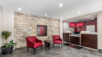 Uma área de recepção de hotel com design moderno, incluindo uma parede de pedra, cadeiras de couro vermelho e um balcão de recepção.