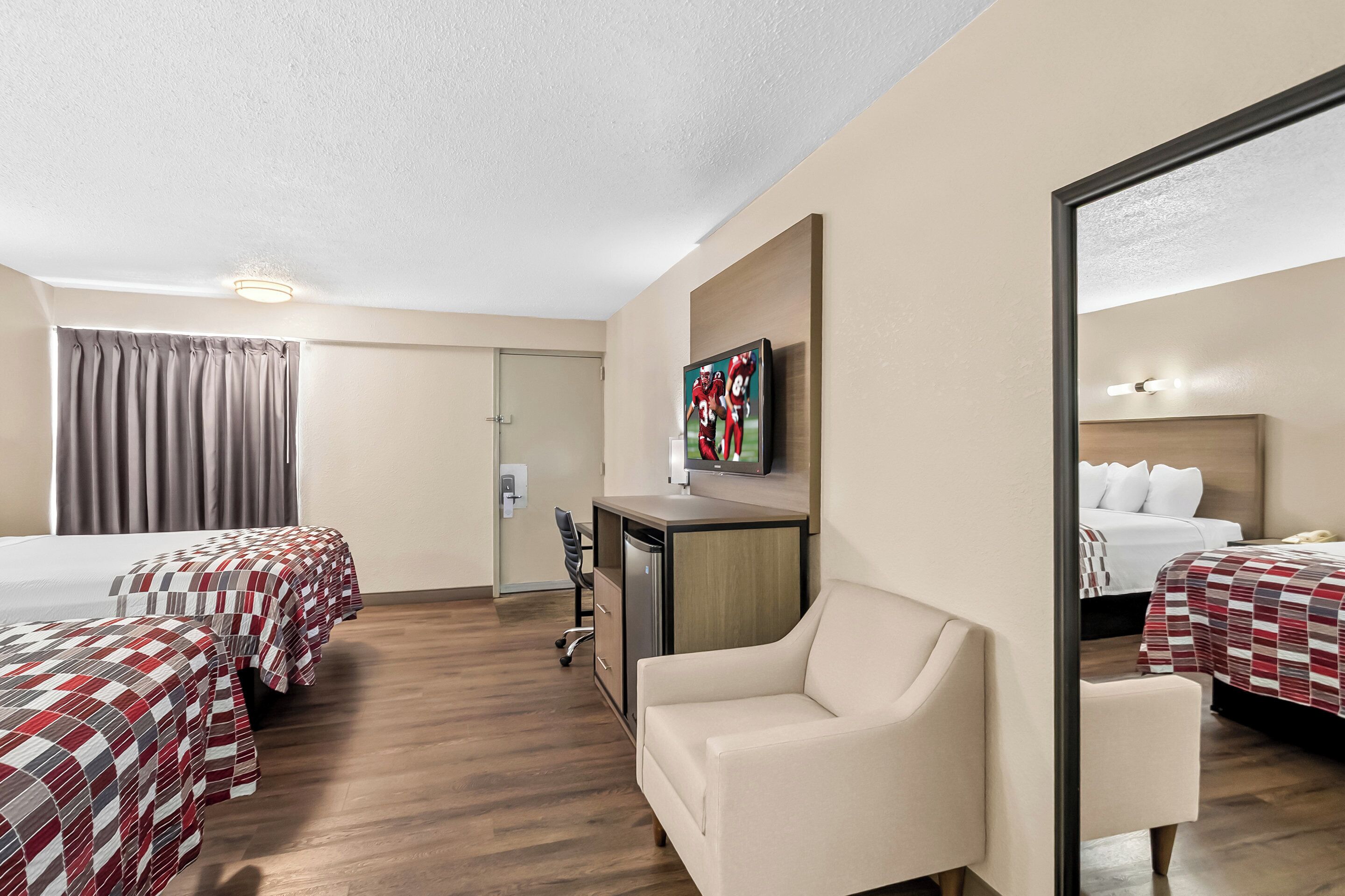 A hotel room with two beds, a desk, a chair, and a TV on the wall.