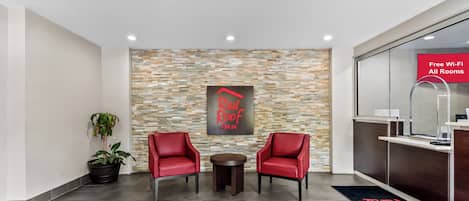 A reception area with a stone wall, two red chairs, a small table, and a potted plant.