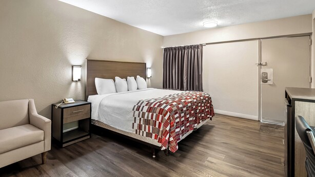 A hotel room with a bed, bedside table, lamp, and a chair. - Red Roof Inn Washington, DC (Washington)