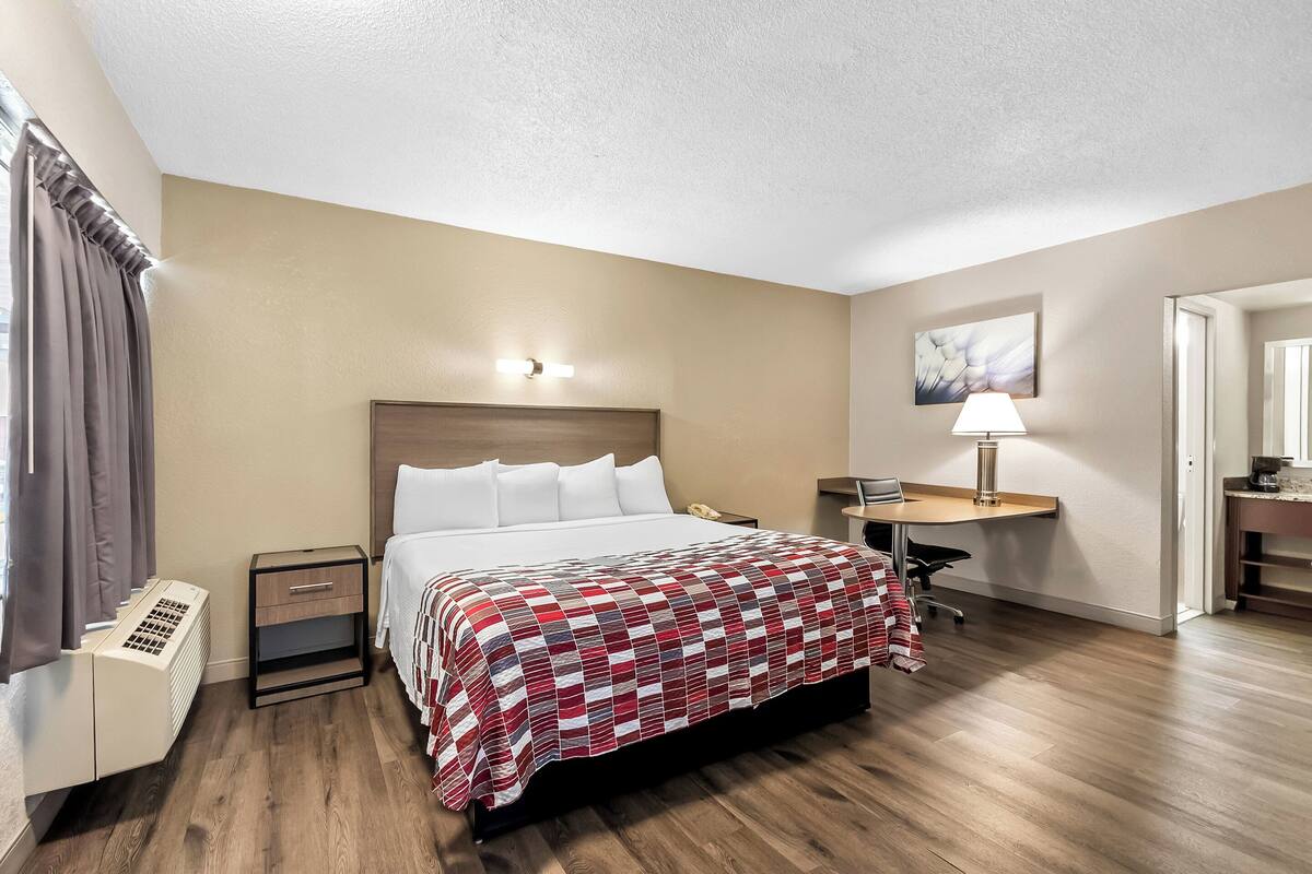 A hotel room with a bed, bedside table, lamp, and a desk with a chair.