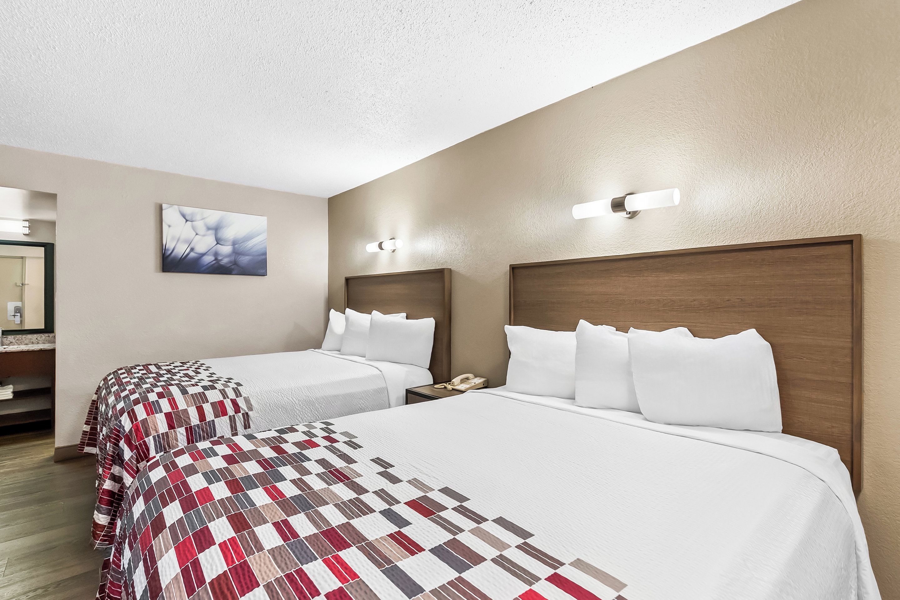 Una habitación de hotel con dos camas, un cabecero de madera, una mesita de noche con un teléfono y un cuadro en la pared.