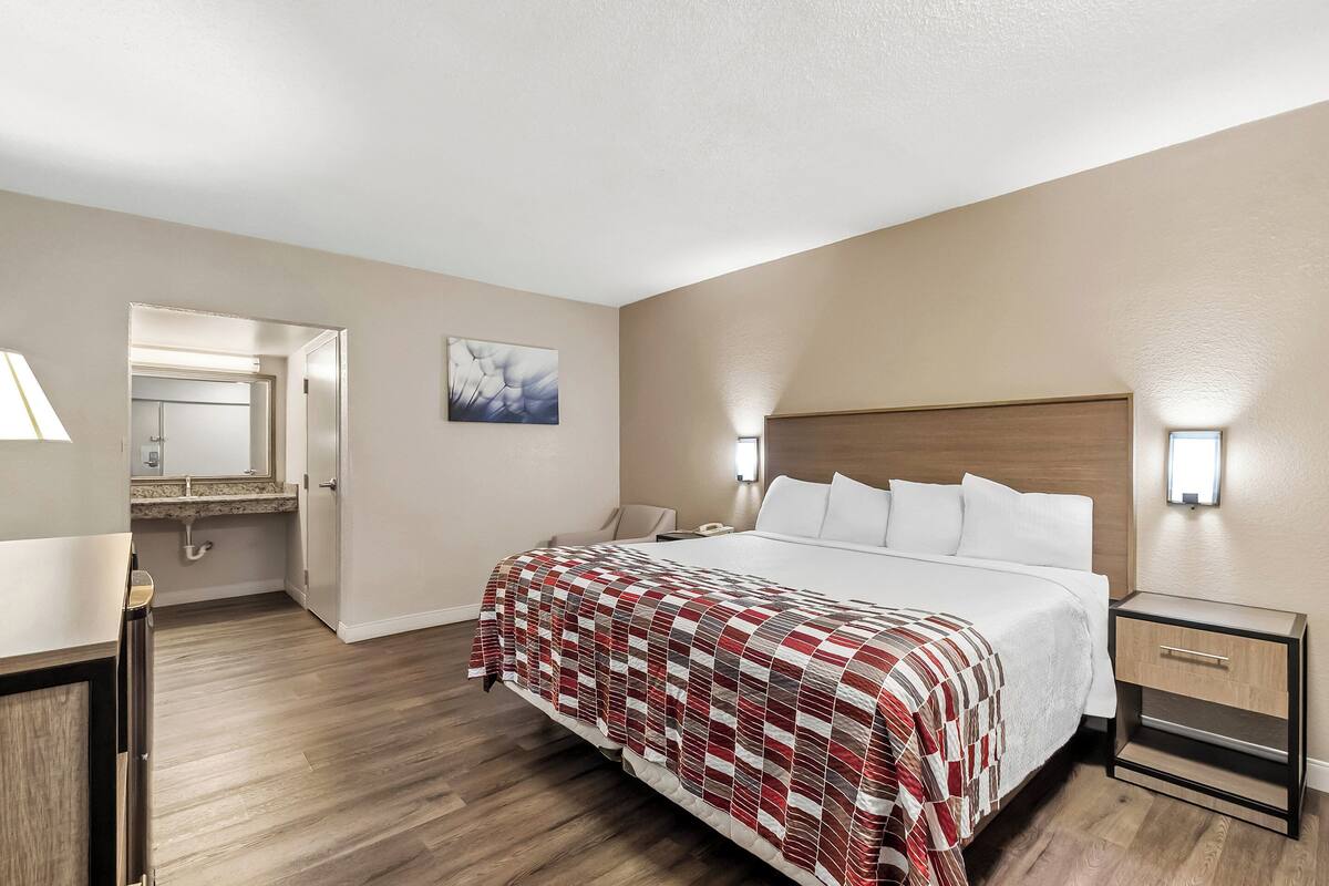 A hotel room with a large bed, bedside tables, a nightstand, a mirror, and a painting on the wall.