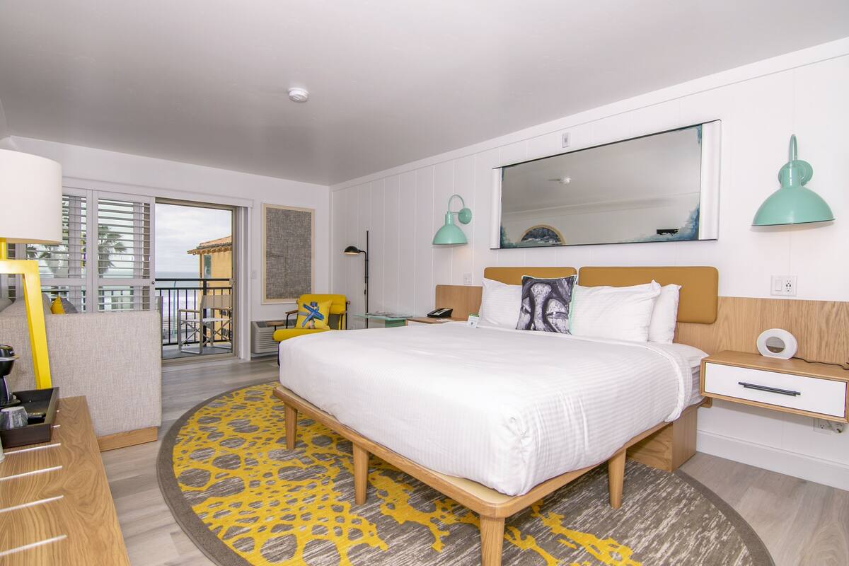 A hotel room with a bed, bedside tables, a mirror, and a view of the outside.