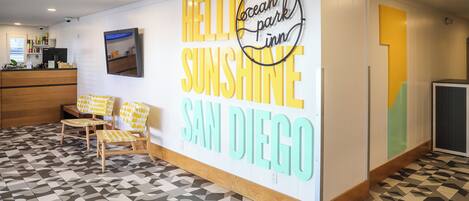Un área de recepción con un gran cartel en la pared que dice 'HELLO SUNSHINE SAN DIEGO' y un cuadro enmarcado sobre el mostrador de recepción.