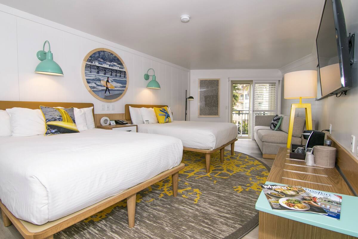A hotel room with two beds, a desk, a chair, a TV, and a window with blinds.