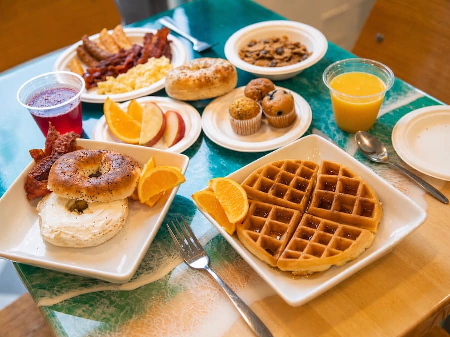 Mesa de café da manhã com pratos de comida, um waffle, fatias de laranja e um copo de suco de laranja.