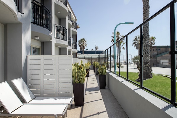 A balcony with white lounge chairs, potted plants, and a view of palm trees and buildings. - Ocean Park Inn (San Diego)