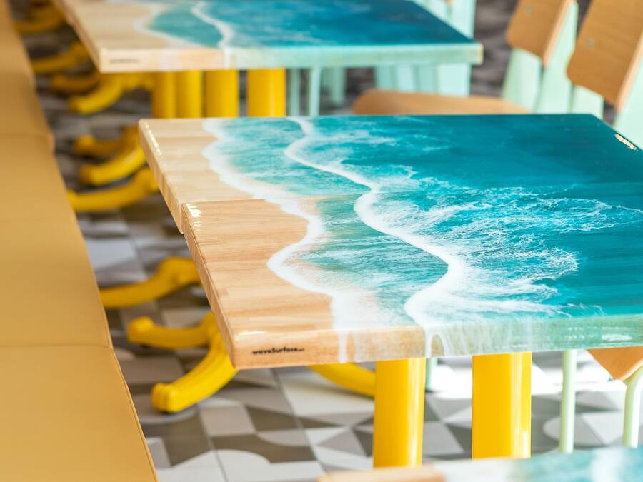Uma mesa comprida com padrão de ondas, rodeada por cadeiras amarelas.