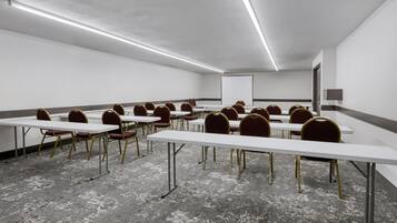 Ein Konferenzraum mit weißen Tischen und Stühlen, Teppichboden und einer Projektionsleinwand.
