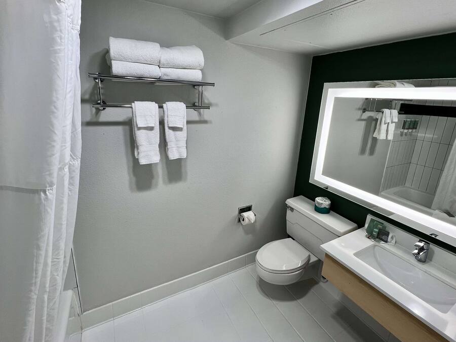 Ein Badezimmer mit Toilette, Waschbecken, Spiegel, Handtuchhalter und einem Regal mit Handtüchern.