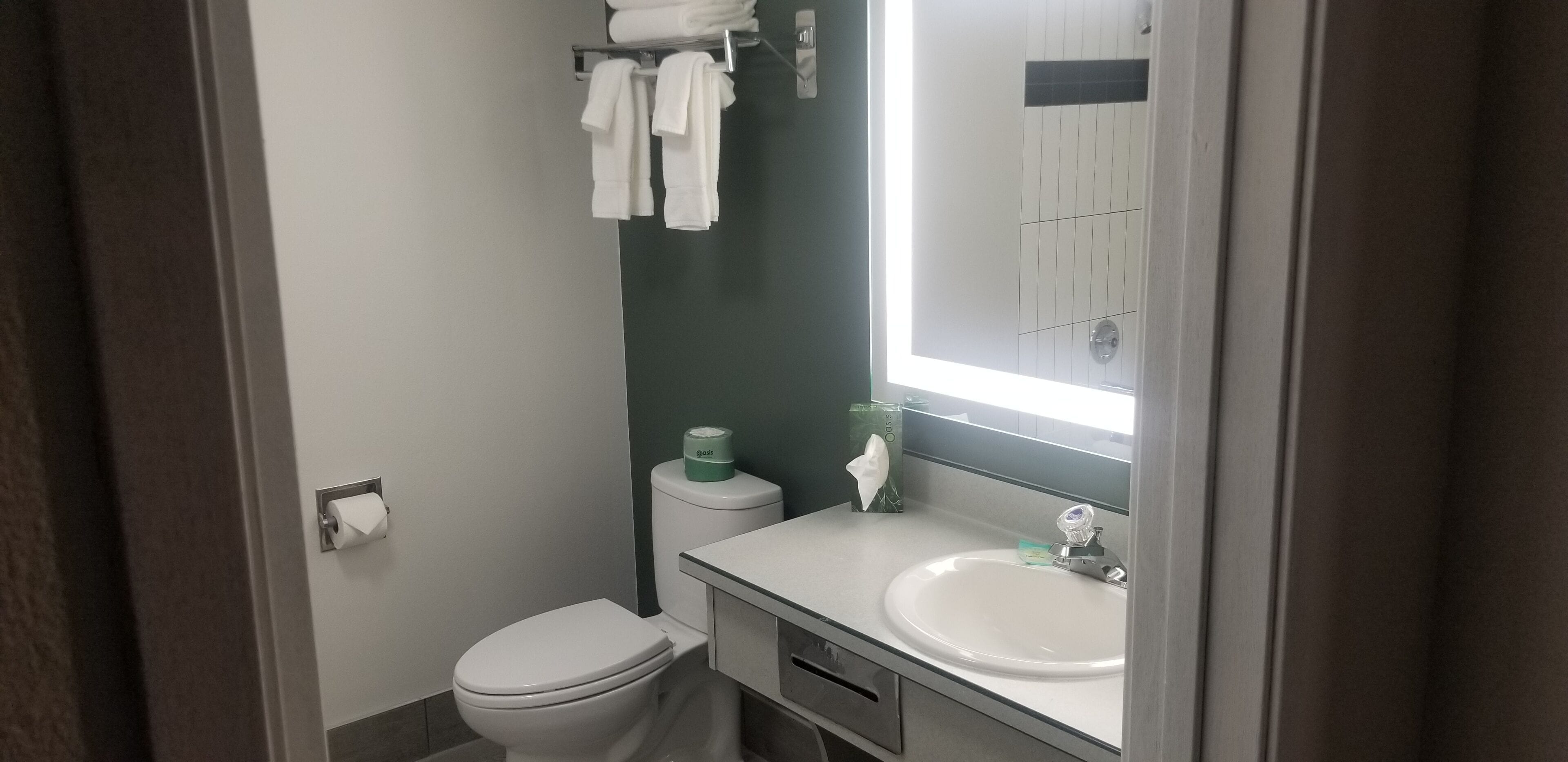 A small bathroom with a toilet, a sink, and a mirror. There are towels hanging on a rack above the toilet.