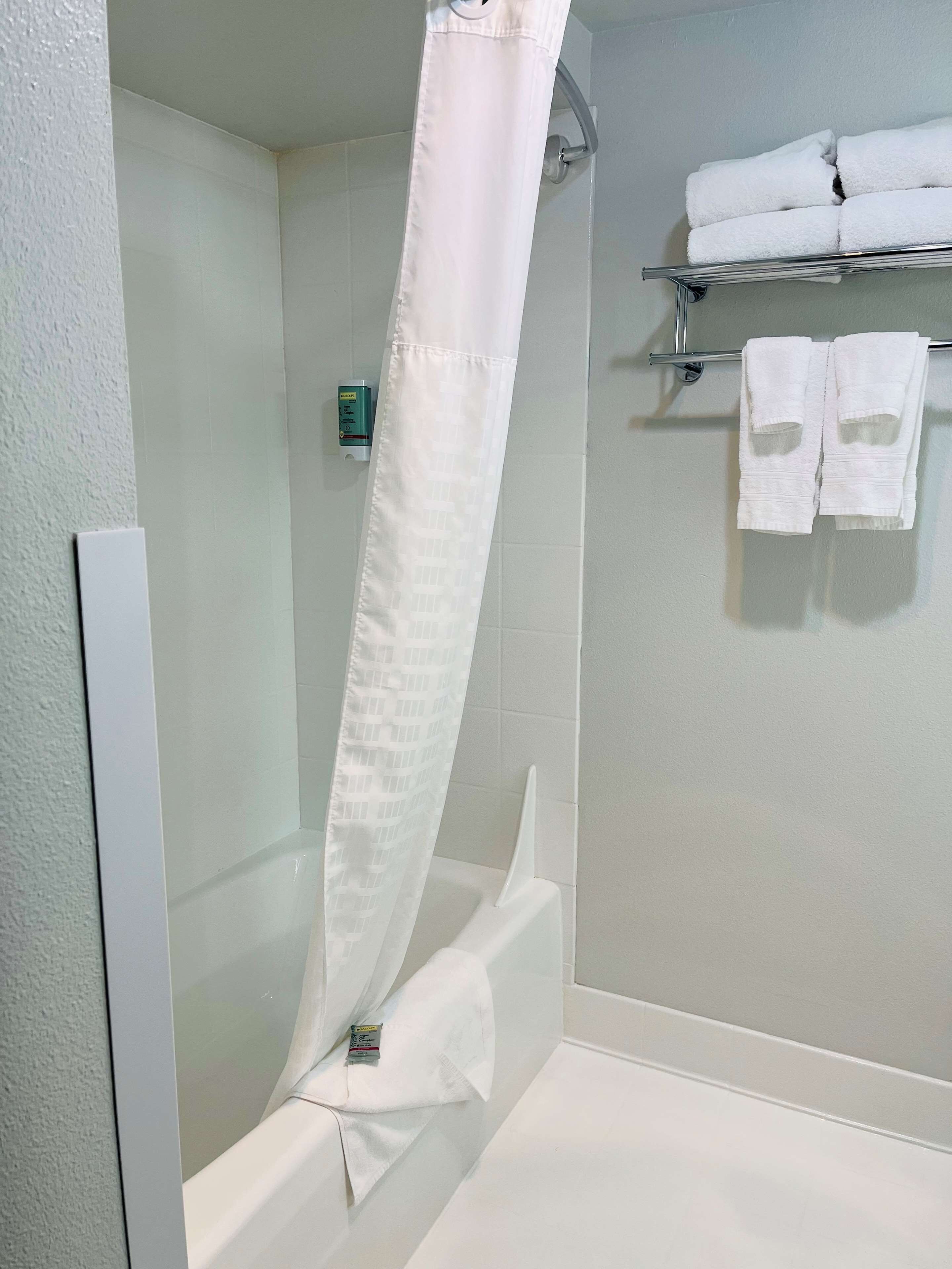 A bathroom with a shower curtain, a towel rack with towels, and a soap dispenser.