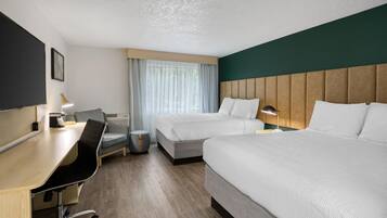 A hotel room with two beds, a desk, a chair, a small table, a lamp, and a television.